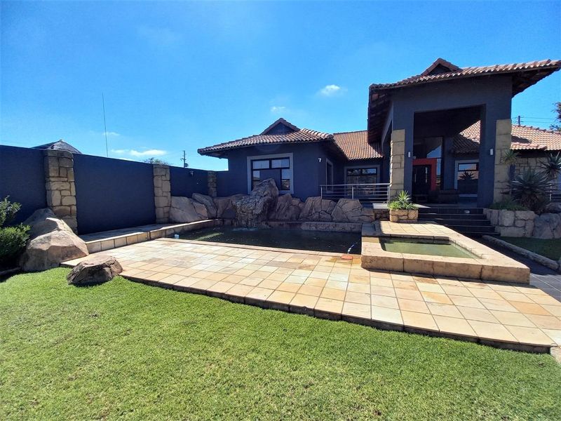 Outdoor pool area featuring a stone water feature, tiled patio, and landscaped garden, set against the rear elevation of the house.