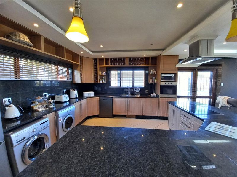 Spacious kitchen featuring granite countertops, extensive wooden cabinetry, built-in oven, extractor fan, and integrated dishwasher with ample workspace.