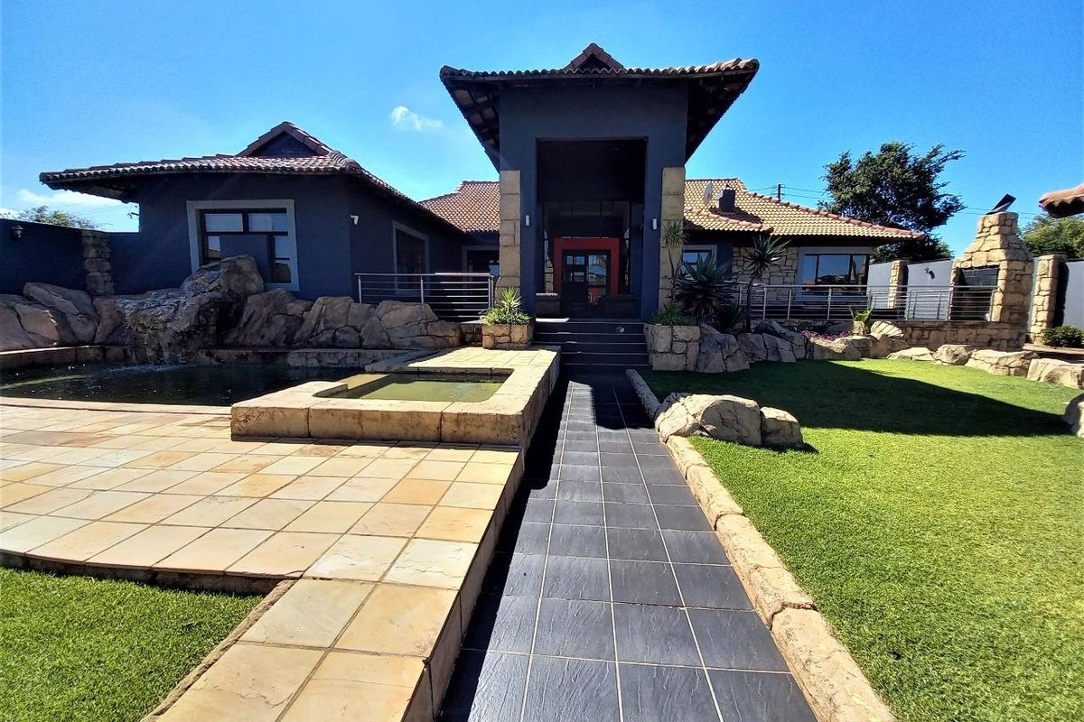 A well-maintained rear exterior featuring a swimming pool, stone-clad water feature, tiled patio area, and a built-in outdoor braai facility.
