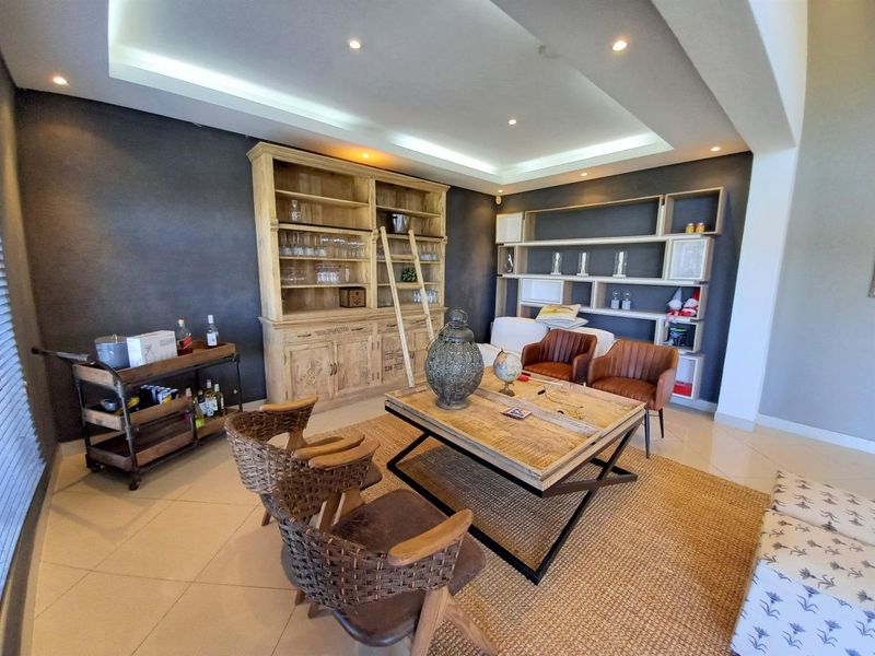 Spacious living room featuring a recessed ceiling with cove lighting, tiled flooring, and extensive built-in shelving units.