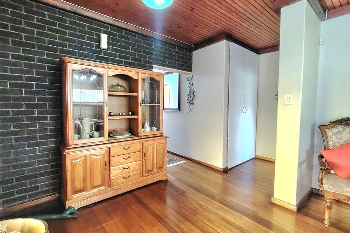 A living area featuring hardwood flooring, a dark exposed brick feature wall, and a timber-paneled ceiling, providing a warm and rustic aesthetic.