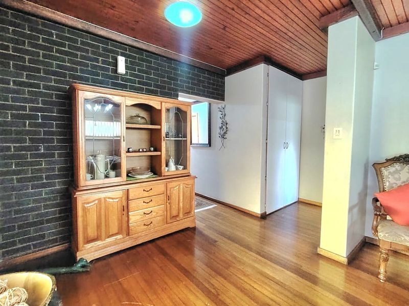 A living area featuring hardwood flooring, a dark exposed brick feature wall, and a timber-paneled ceiling, providing a warm and rustic aesthetic.
