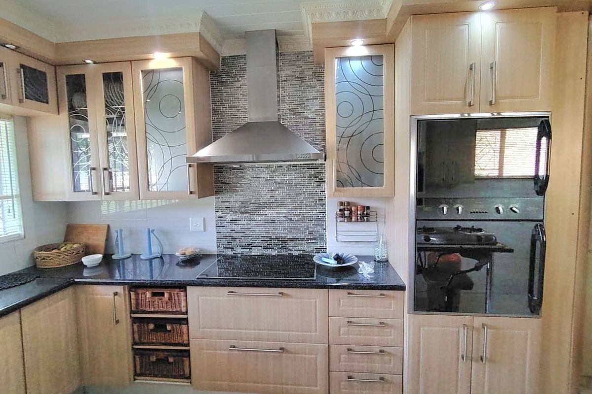 A well-maintained kitchen featuring light wood cabinetry, granite countertops, a mosaic tile backsplash, and integrated stainless steel appliances.