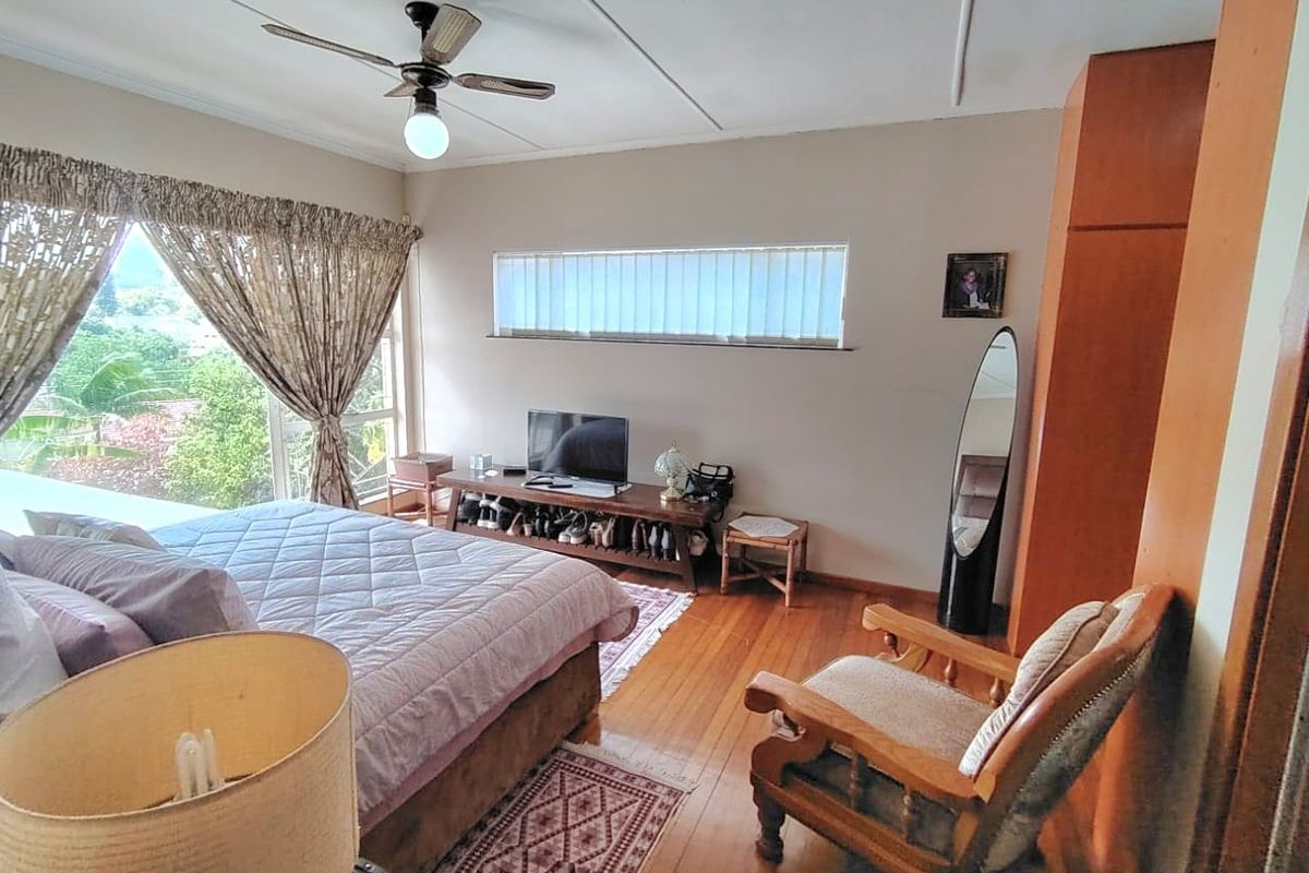 A bedroom featuring hardwood flooring, a ceiling fan, and built-in wardrobe storage with natural light from large windows.