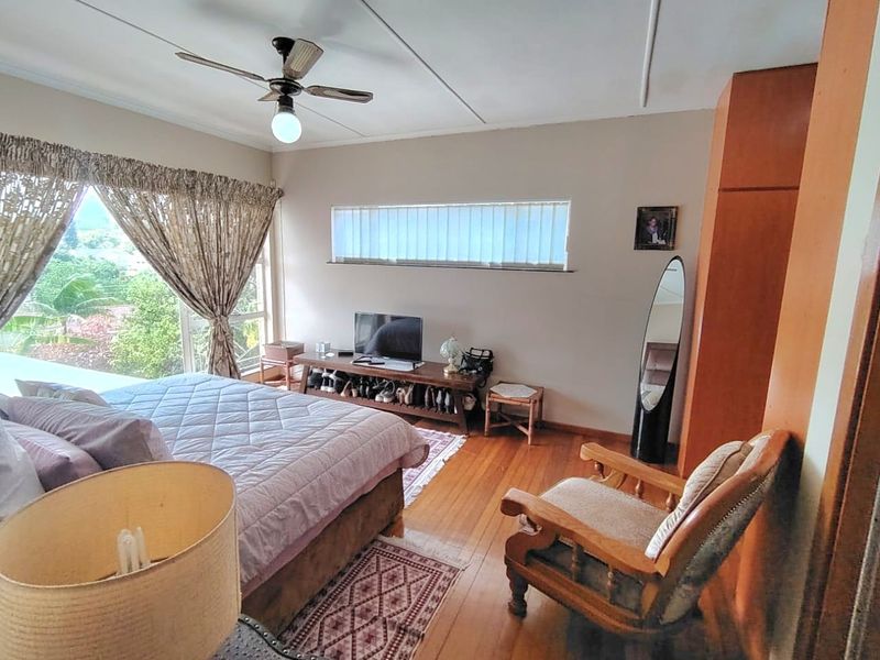 A bedroom featuring hardwood flooring, a ceiling fan, and built-in wardrobe storage with natural light from large windows.