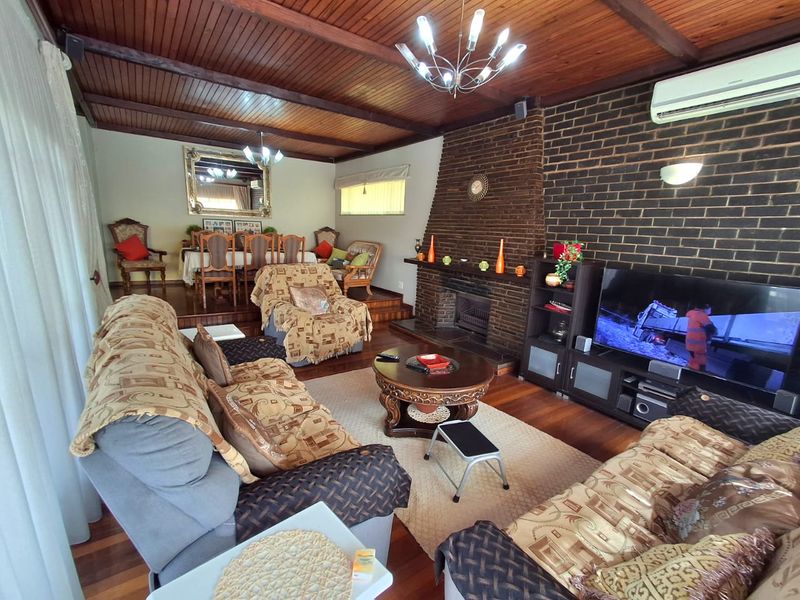 Spacious open-plan living and dining area featuring a prominent brick fireplace, warm timber ceilings, and polished hardwood flooring with a raised dining section.
