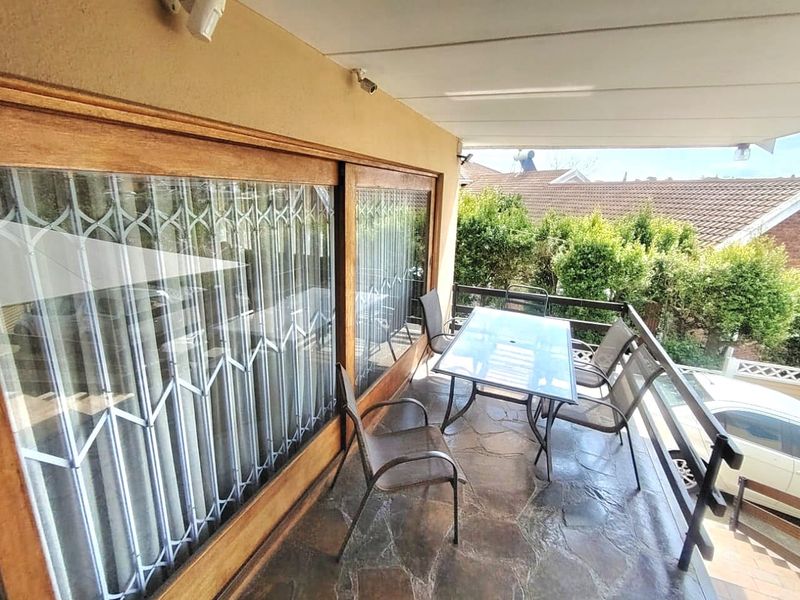 A covered balcony featuring stone flooring, sliding glass doors with security gates, and a protective railing overlooking the surrounding area.