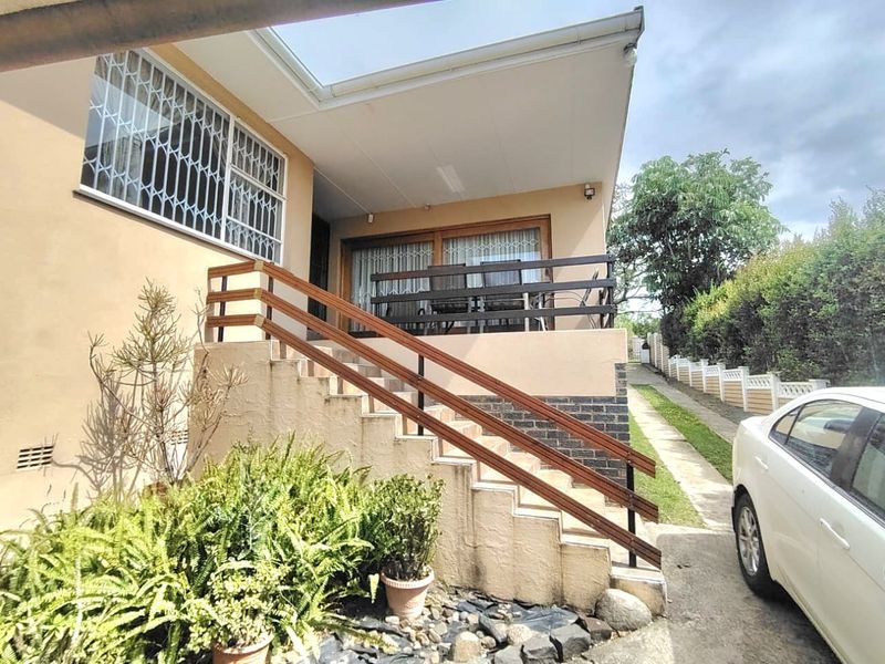 A covered patio area featuring a concrete staircase with timber handrails, providing access to the main entrance through sliding glass doors.
