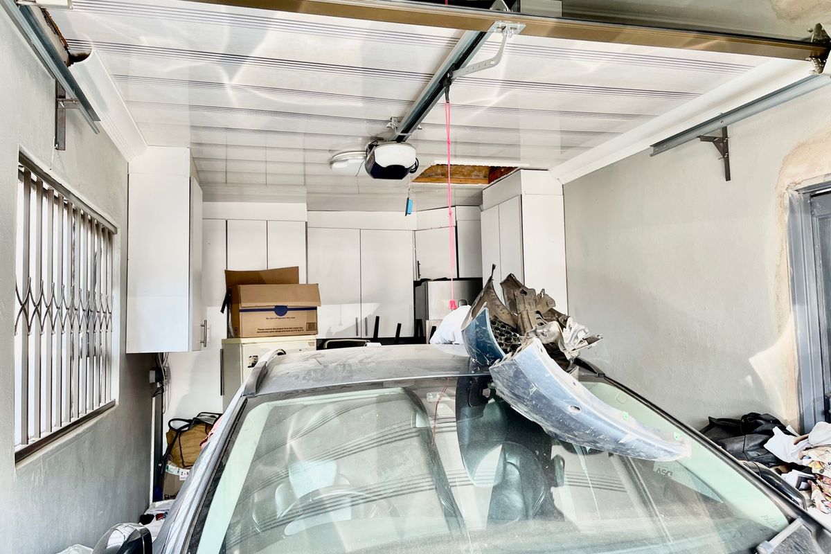 A functional garage space featuring built-in storage cabinetry, a motorized garage door system, and security bars on the window.