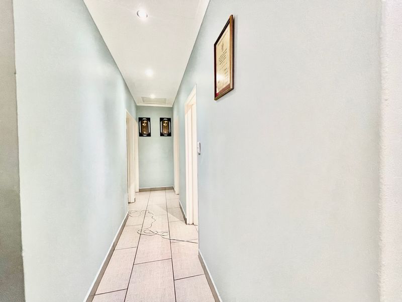 A clean, well-lit hallway featuring neutral tiled flooring and recessed downlighting, providing access to multiple rooms within the home.