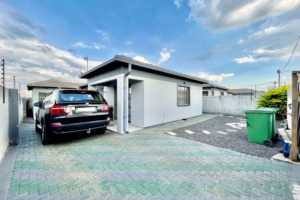 Front view of a modern single-story house featuring a paved driveway, secure perimeter wall with electric fencing, and a tiled roof.
