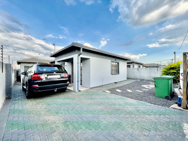 Front view of a modern single-story house featuring a paved driveway, secure perimeter wall with electric fencing, and a tiled roof.