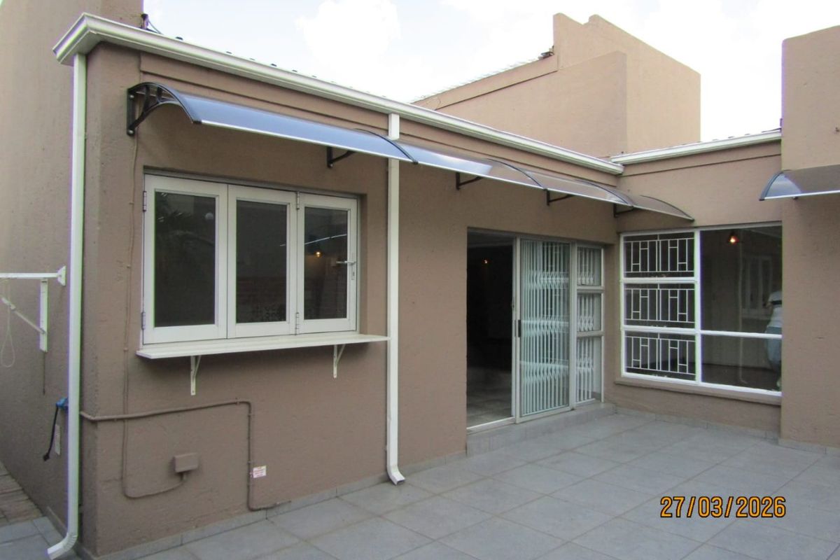 Rear exterior view featuring a paved patio area, sliding glass doors, security bars on windows, and protective polycarbonate awnings.