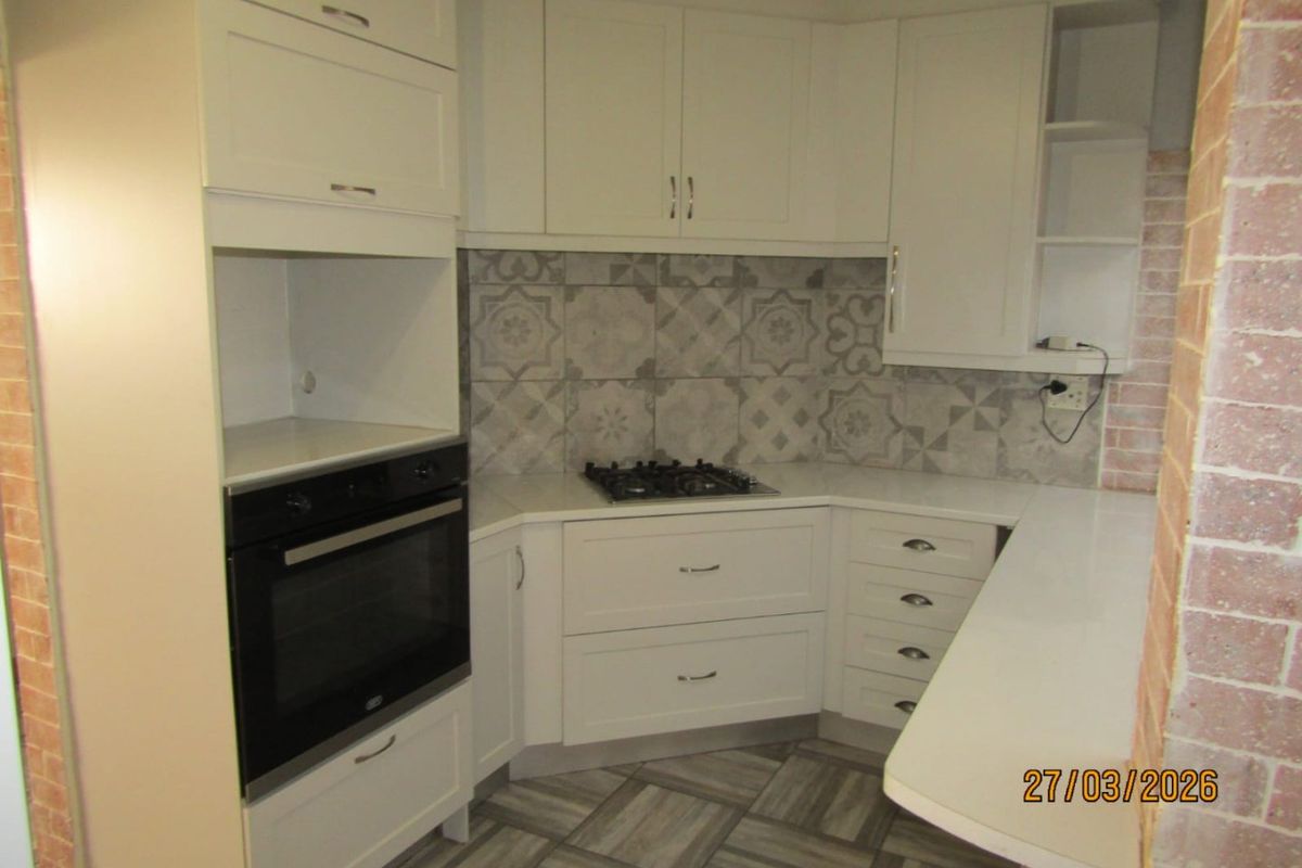 Modern kitchen featuring white cabinetry, stone countertops, a built-in oven, gas hob, and decorative patterned tile backsplash.