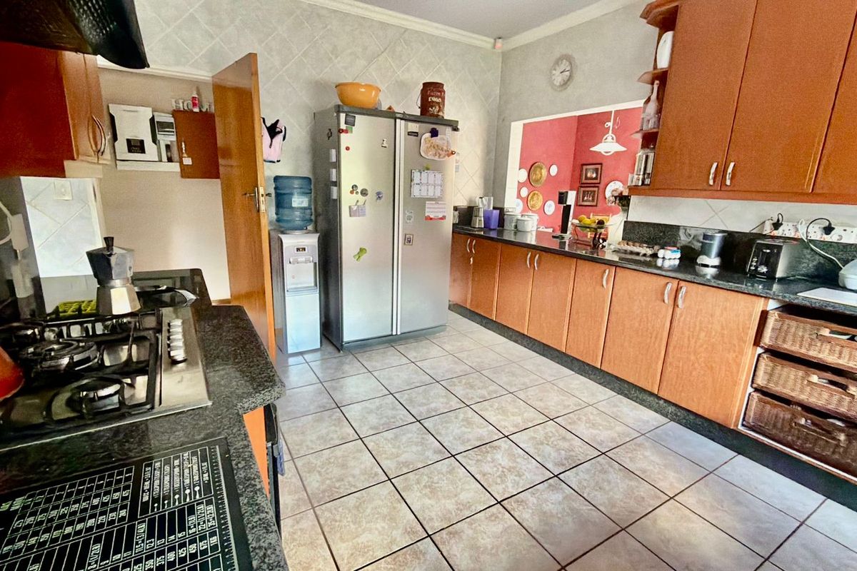 A functional kitchen featuring wooden cabinetry, granite countertops, a gas hob with extractor fan, and tiled flooring throughout.