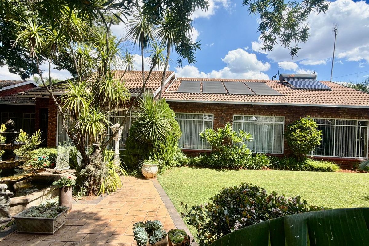 Rear view of the house featuring a brick facade, tiled roof with solar panels, a paved patio area, and a landscaped garden with water feature.