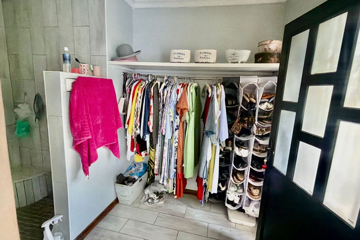 A bedroom walk-in closet area featuring built-in shelving, a hanging rail, and tiled flooring, accessible via a glass panel door.