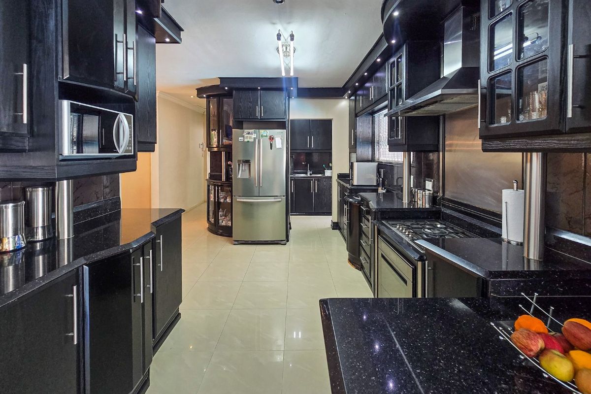 Modern kitchen featuring dark cabinetry, granite countertops, integrated appliances, gas hob, and tiled flooring in a spacious, well-lit layout.