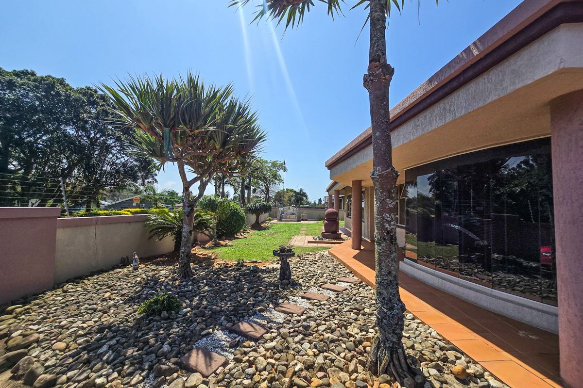 A well-maintained rear garden featuring a tiled patio, paved pathways, established trees, and secure boundary walls with electric fencing.