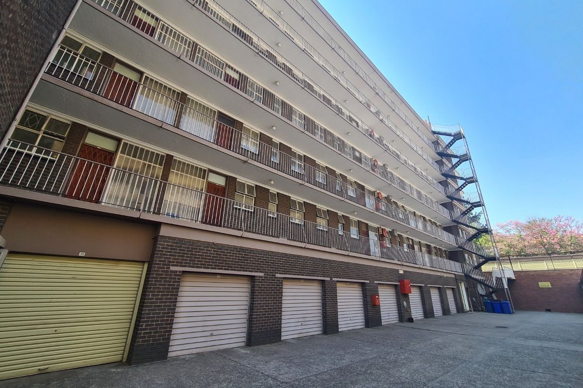 Rear view of a multi-story commercial or residential building featuring ground-level roller shutter garages, external fire escape stairs, and balcony access.
