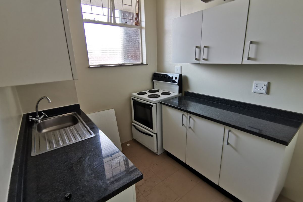 A functional kitchen featuring white cabinetry, dark granite countertops, a stainless steel sink, and a freestanding stove, with tiled flooring throughout.