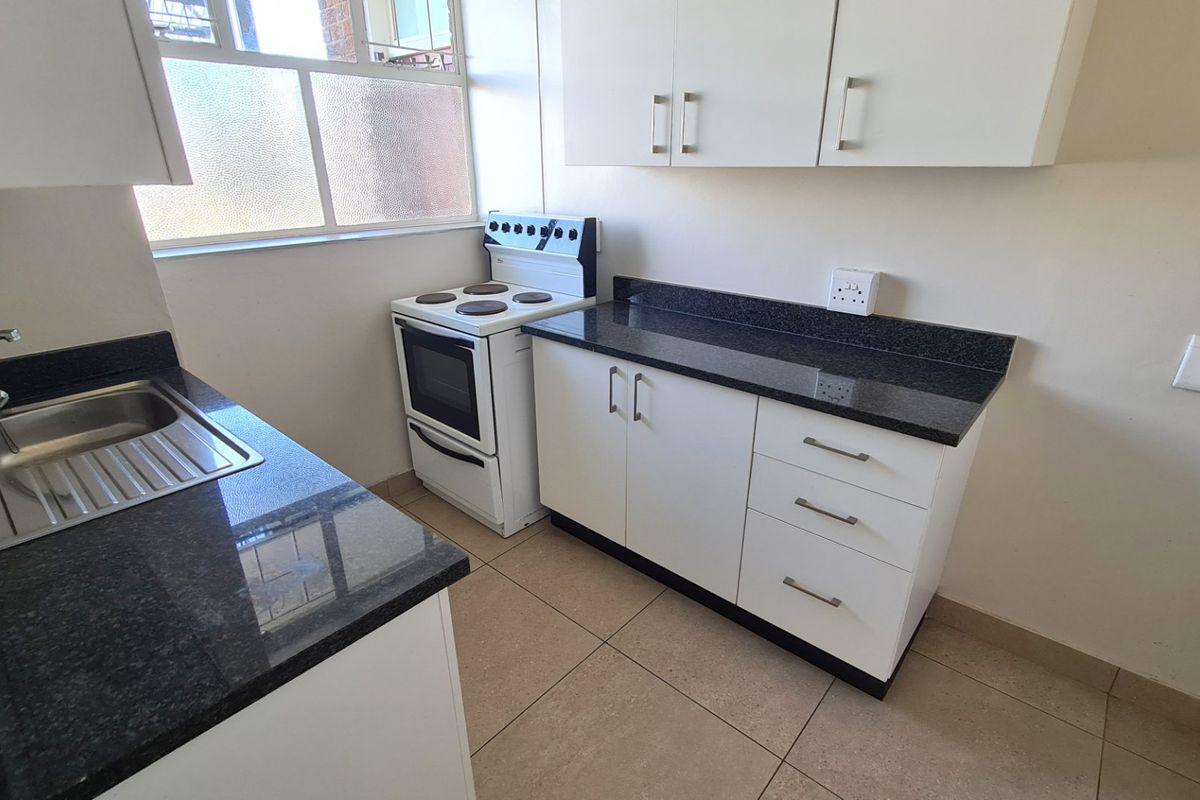 A clean, functional kitchen featuring white cabinetry, dark granite countertops, a stainless steel sink, and a freestanding stove with tiled flooring.