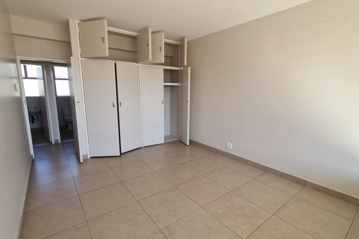 A vacant bedroom featuring neutral tiled flooring and built-in cupboards with overhead storage, providing a clean and functional space.
