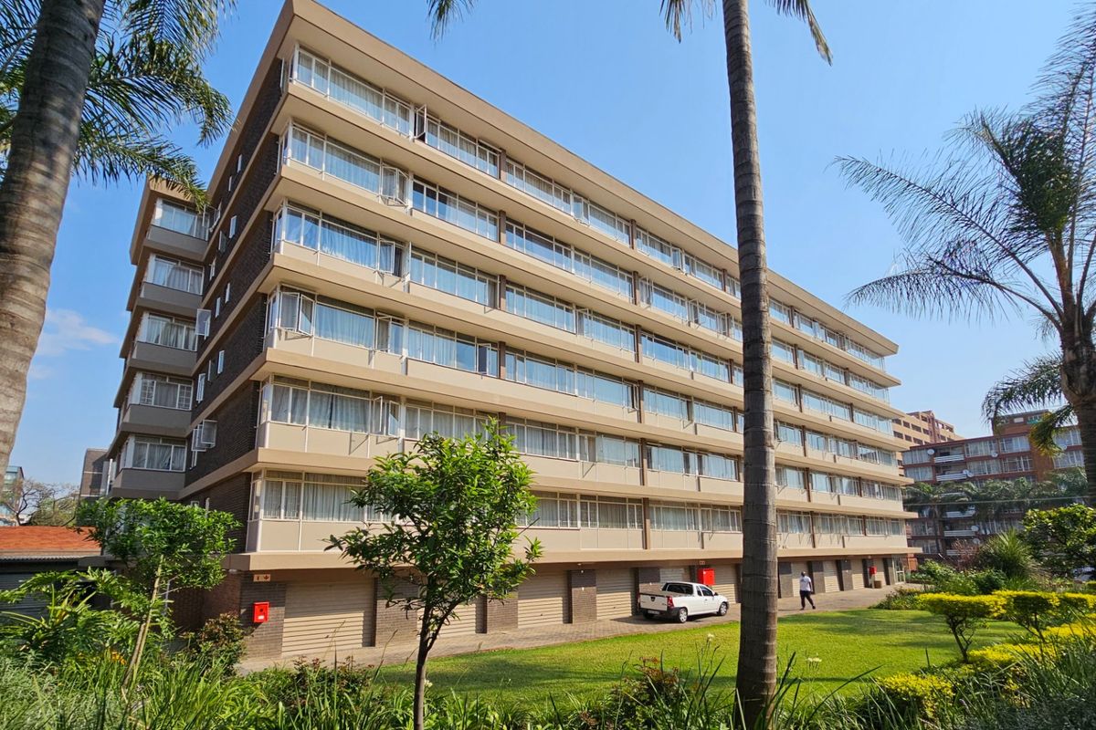 A multi-story commercial or residential building featuring a clean facade with large windows, ground-level garage access, and well-maintained surrounding garden areas.