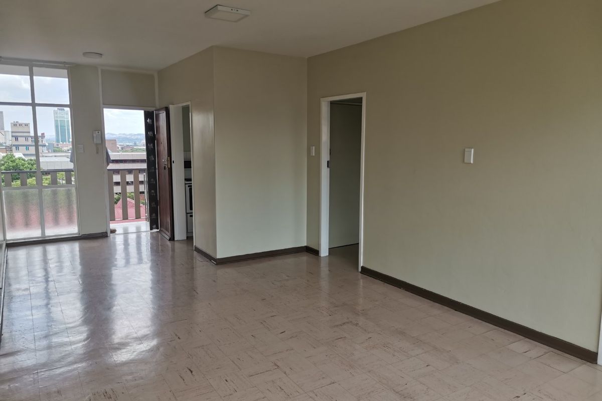 An empty, open-plan living area featuring vinyl tile flooring, neutral wall tones, and direct access to an outdoor balcony.