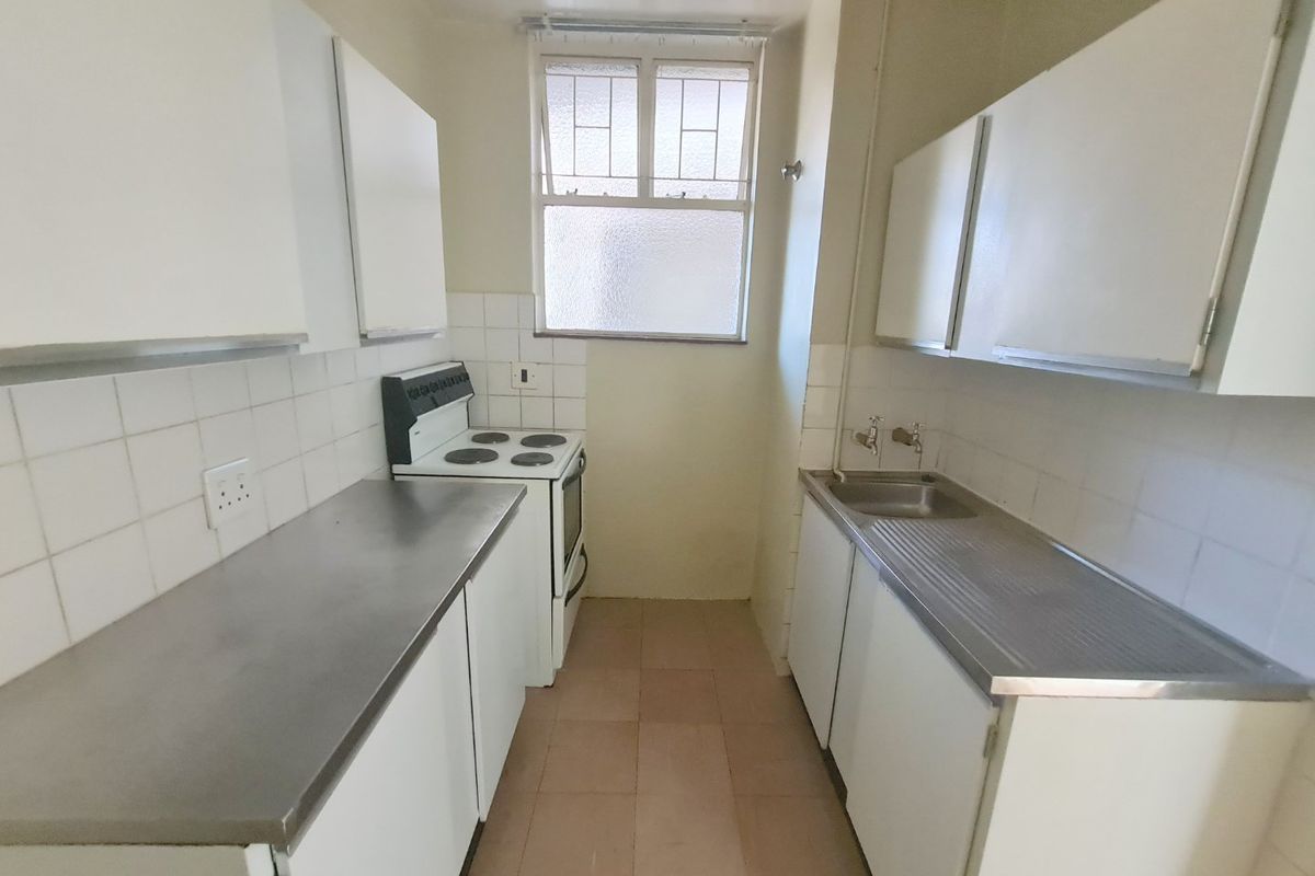 A compact, functional kitchen featuring built-in cabinetry, a stainless steel sink, and an electric stove with tiled backsplash and flooring.