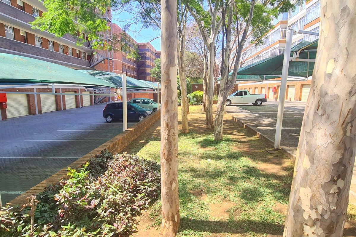 Exterior view of a commercial property featuring covered parking bays, paved driveway, and a landscaped garden area between building blocks.