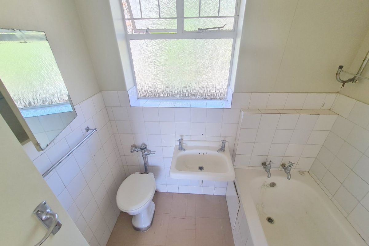 A dated bathroom featuring a standard bathtub, wall-mounted basin, and flush toilet, finished with white wall tiles and a leaded glass window.
