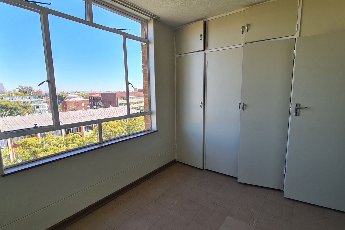 An empty bedroom featuring built-in cupboards, large windows with city views, and tiled flooring, offering a blank canvas for renovation.