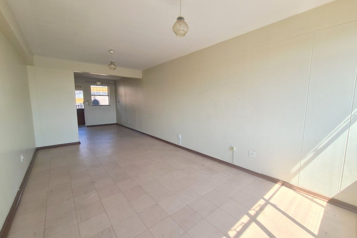 An empty, open-plan living area featuring tiled flooring and simple pendant lighting, offering a blank canvas for renovation or interior design updates.
