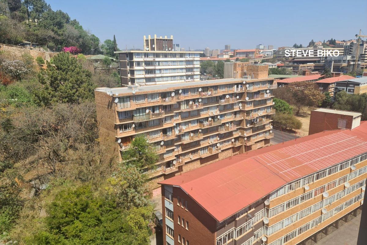 An elevated aerial view of a residential apartment complex featuring multiple buildings with balconies, metal roofing, and surrounding mature trees.