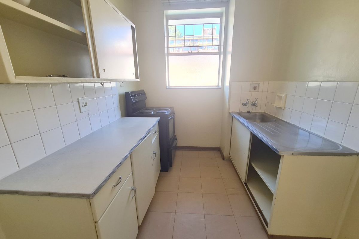 A compact, dated kitchen featuring original cabinetry, a stainless steel sink, tiled backsplash, and a freestanding stove, offering potential for modernization.