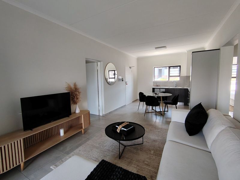 Modern open-plan living area featuring tiled floors and a functional kitchen space with built-in cabinetry and a stainless steel sink.