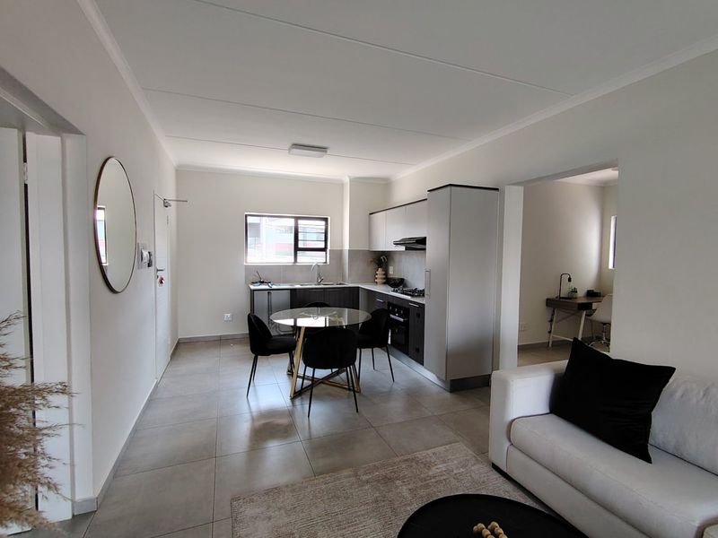 Modern open-plan kitchen and living area featuring sleek cabinetry, integrated appliances, and neutral tiled flooring, creating a bright and functional living space.