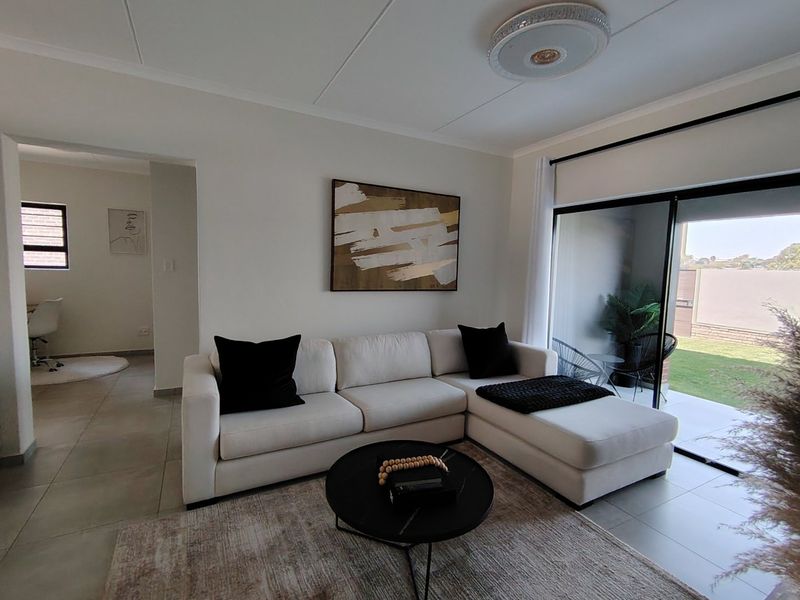 A bright and modern living room featuring tiled flooring and a large sliding glass door that provides seamless access to the outdoor patio area.