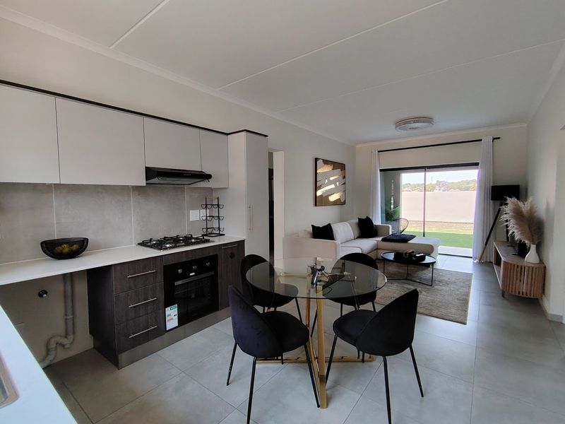 Modern open-plan living area featuring a contemporary kitchen with built-in appliances, tiled flooring, and seamless access to an outdoor patio through sliding glass doors.