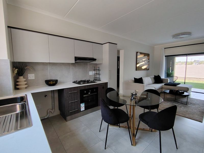 Modern open-plan kitchen and living area featuring sleek cabinetry, integrated appliances, tiled flooring, and direct access to an outdoor patio through sliding glass doors.