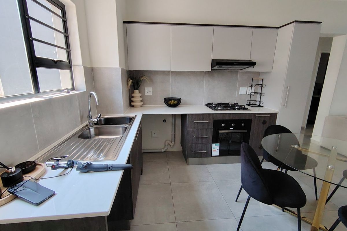 Modern kitchen featuring sleek cabinetry, a gas hob, built-in oven, extractor fan, and a stainless steel double sink with tiled finishes.