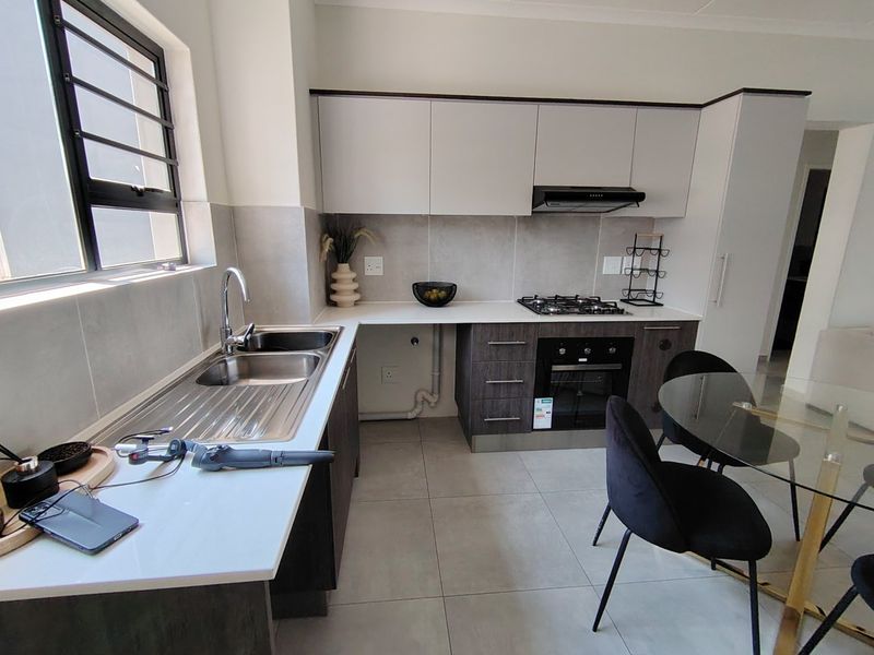 Modern kitchen featuring sleek cabinetry, a gas hob, built-in oven, extractor fan, and a stainless steel double sink with tiled finishes.