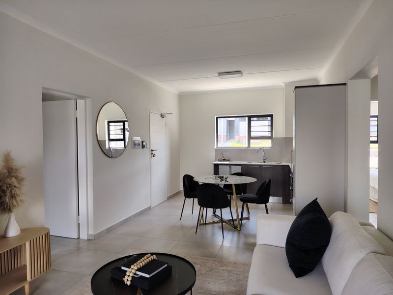 An open-plan living and dining area featuring modern tiled flooring, neutral walls, and a compact kitchen with built-in cabinetry and sink.