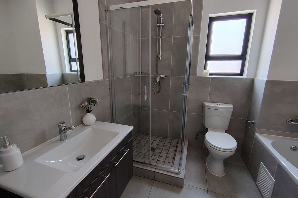 Modern bathroom featuring a vanity with basin, glass-enclosed shower, toilet, and a bathtub with neutral grey wall and floor tiling.