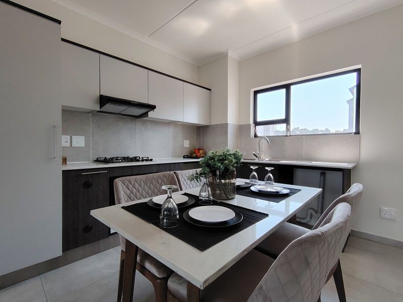 Modern open-plan kitchen and dining area featuring sleek cabinetry, a gas hob, extractor fan, and tiled finishes with a bright window.
