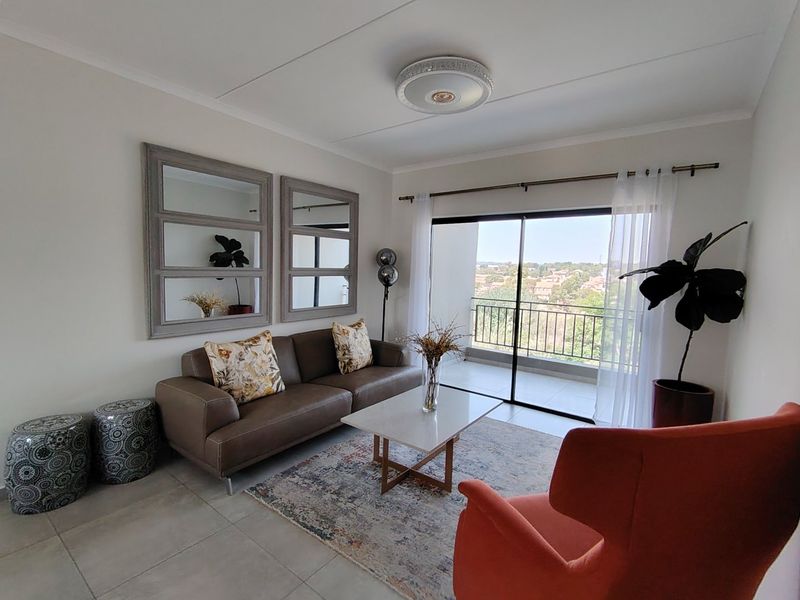 A bright and well-maintained living room featuring tiled floors, a modern ceiling light, and large sliding glass doors leading to a balcony with scenic views.