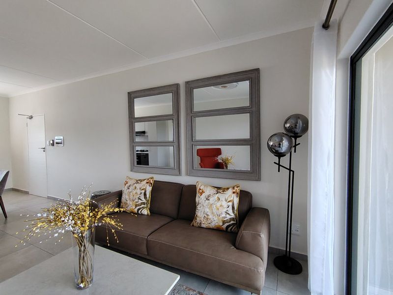 A bright and well-maintained living room featuring neutral tiled flooring and a large sliding glass door providing access to the exterior.