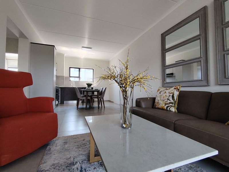 An open-plan living and dining area featuring tiled floors and a modern kitchen with built-in cabinetry and appliances.