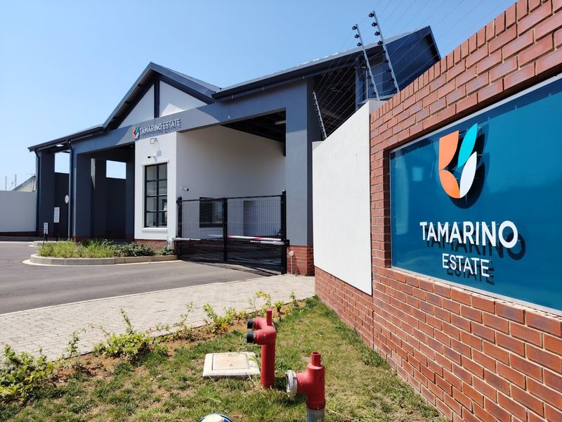 The entrance to Tamarino Estate featuring a modern security gatehouse, paved driveway, and brick boundary wall with integrated estate signage.